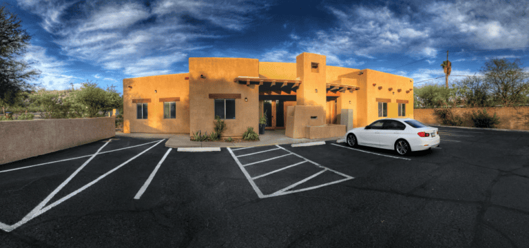 Exterior view of Arizona Psychiatry's office building, a modern adobe-style structure with a spacious parking lot under a blue sky.